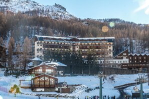 A multi-story hotel with balconies, a ski lift, and a mountainous backdrop.