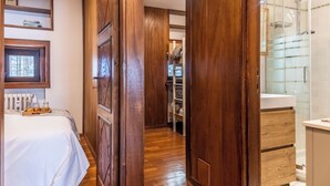 Camera d'albergo con un armadio in legno, un letto con un vassoio di pane, un bagno bianco con cabina doccia in vetro e vista sull'esterno.