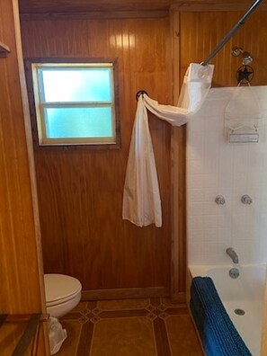 Un baño de madera con inodoro, ducha y ventana.