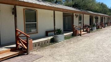 A row of motel rooms with individual entrances, outdoor seating, and a gravel driveway.