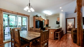 A spacious dining area with a large wooden table and chairs, a kitchen with wooden cabinets, and a view through large windows. - Spacious Cabin with Indoor and Outdoor Swimming Pool in Branson, Missouri (Branson)