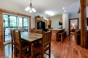 A spacious dining area with a large wooden table and chairs, a kitchen with wooden cabinets, and a view through large windows. - Spacious Cabin with Indoor and Outdoor Swimming Pool in Branson, Missouri (Branson)