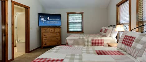 A bedroom with two beds, a dresser, a television, and a window with blinds.