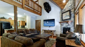 A spacious living room with a large sectional sofa, a fireplace, a stone wall, and a mounted buffalo head. - Spacious Cabin with Indoor and Outdoor Swimming Pool in Branson, Missouri (Branson)