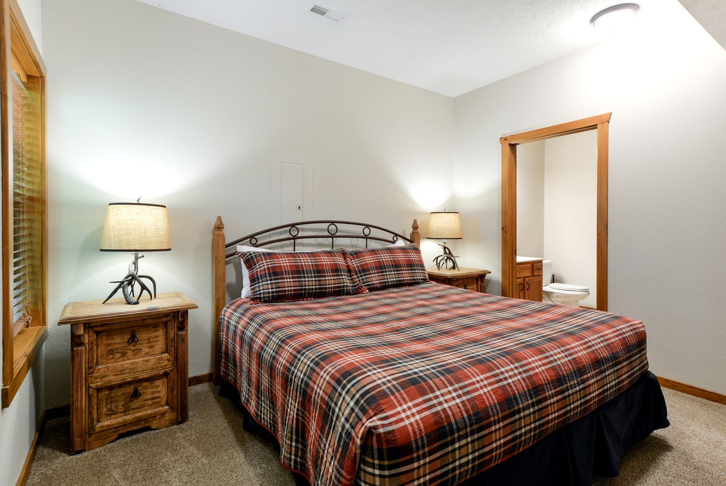 Un dormitorio con una cama, dos mesitas de noche con lámparas, una mesita auxiliar de madera, un espejo y una puerta.