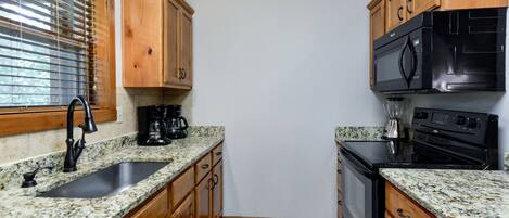 A compact kitchen with wooden cabinets, granite countertops, a black stove, and a coffee maker.
