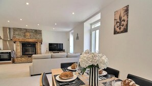 Een moderne woonkamer met een open haard, een eetgedeelte met een tafel gedekt voor twee personen, en een bank.