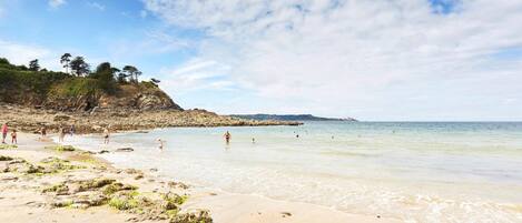 Una spiaggia con acque cristalline, costa rocciosa e persone che nuotano.
