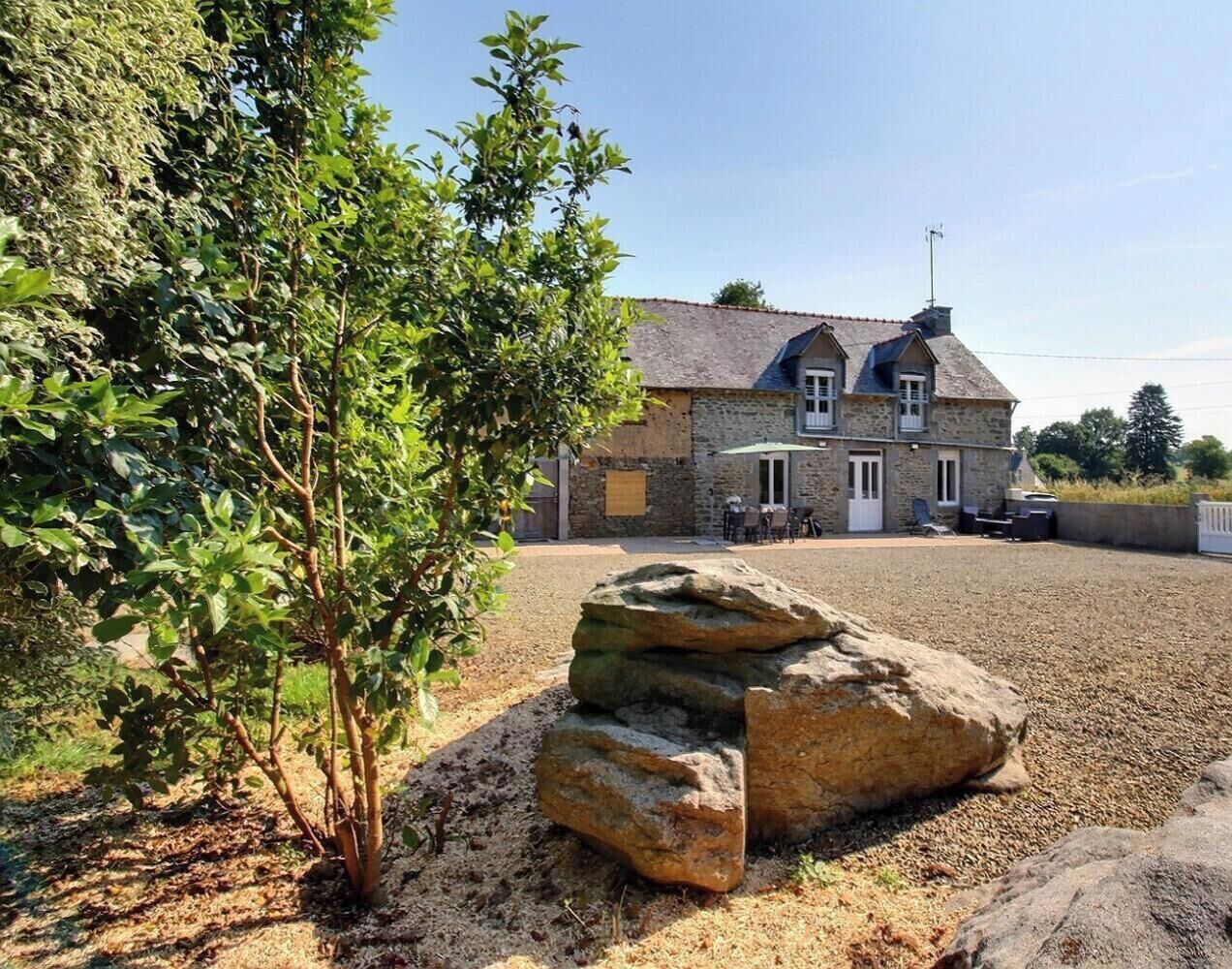 A stone building with a gravel driveway, a tree, and a large rock.