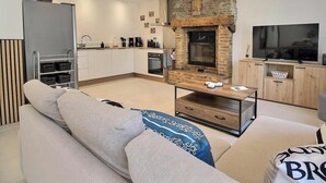 Een moderne woonkamer met een open haard, een bank, een salontafel en een keuken in de verte.