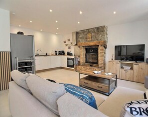 A modern living room with a fireplace, sofa, coffee table, and kitchen area in the background. - From the rock - LE MENE (LE MENE)