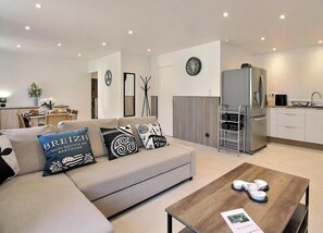 A modern living room with a sofa, coffee table, and kitchen area with appliances. - From the rock - LE MENE (LE MENE)