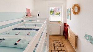 Een kinderkamer met stapelbedden, een raam met uitzicht, een radiator en een hopscotch vloerkleed.