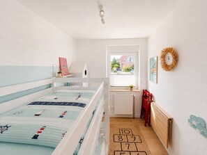 A child's bedroom with bunk beds, a window with a view, a radiator, and a hopscotch rug. - Kellenquartier – Anker 8 | Newly renovated, family-friendly, with a garden (Kellenhusen (Ostsee))