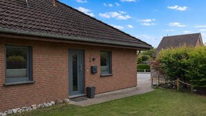 Een bakstenen huis met pannendak, een voordeur en een kleine voortuin met een bankje en een boom.