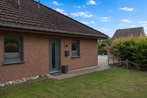 A brick house with a tiled roof, a front door, and a small front yard with a bench and a tree. - Kellenquartier – Anker 8 | Newly renovated, family-friendly, with a garden (Kellenhusen (Ostsee))