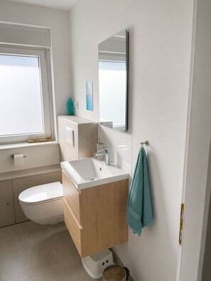 A modern bathroom with a toilet, sink, mirror, and window. - Kellenquartier – Anker 8 | Newly renovated, family-friendly, with a garden (Kellenhusen (Ostsee))