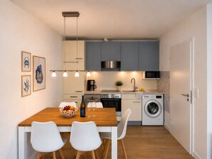 A compact kitchen with a dining table, chairs, a washing machine, and a microwave. - Kellenquartier – Anker 8 | Newly renovated, family-friendly, with a garden (Kellenhusen (Ostsee))