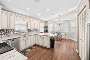 A modern kitchen with a dishwasher, granite countertops, and a dining area with a chandelier.