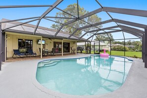 A covered swimming pool with a patio area, lounge chairs, and a pink floatation device.