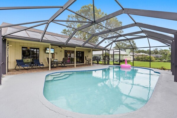 A covered swimming pool with a patio area, lounge chairs, and a pink floatation device.