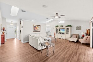 A spacious living room with a white sofa, a glass coffee table, and a television set.