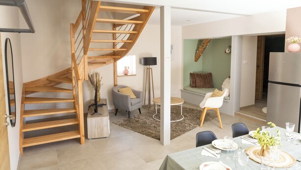 En modern inredning med en spiralformad trappa i trä, en matplats med ett bord dukat för två personer och en sittgrupp med en soffa och fåtöljer.