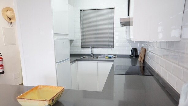 Una cocina moderna con armarios blancos, un lavamanos doble, una ventana con persianas y una cafetera.
