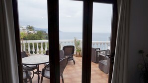 Un balcón con una mesa y sillas, una planta en maceta y vistas al mar.