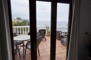Ein Balkon mit Tisch, Stühlen, einem Blumentopf und Blick aufs Meer.