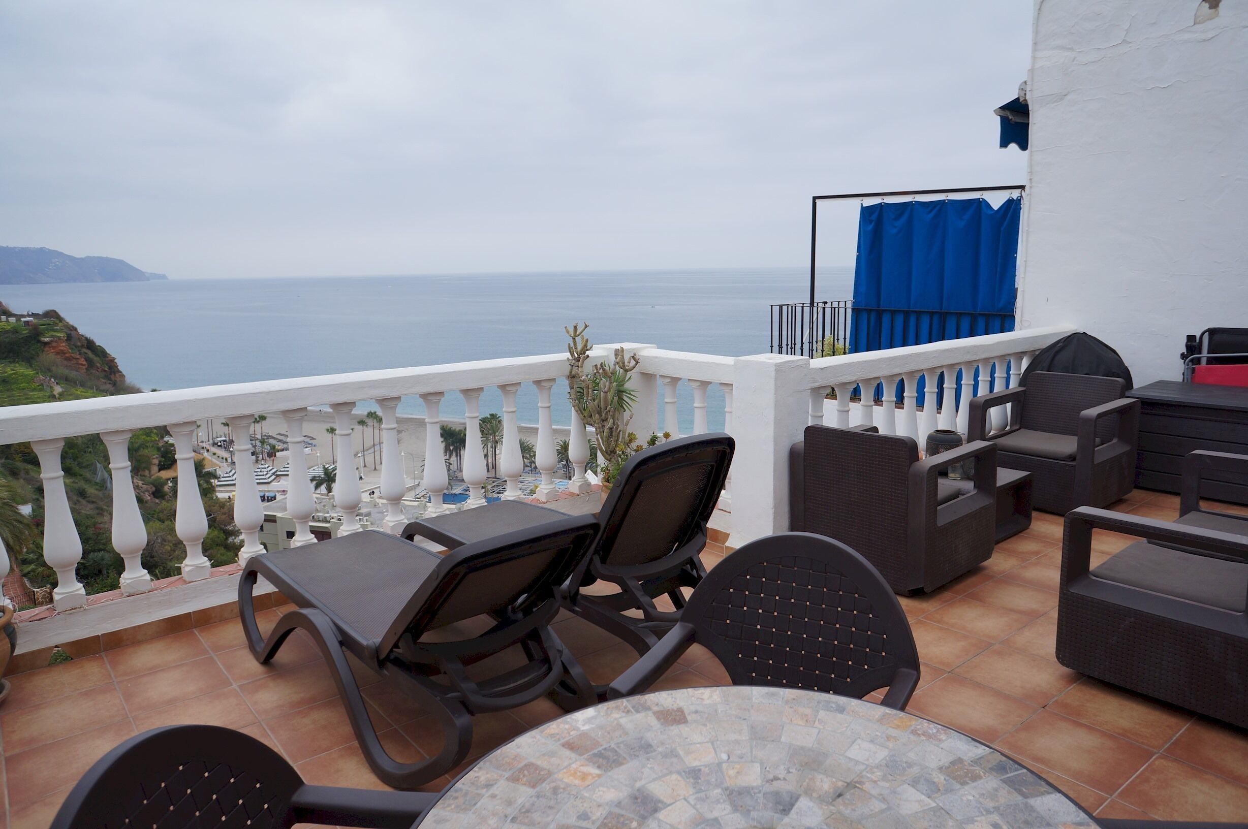 A terrace with outdoor furniture, a view of the sea, and a white balustrade.