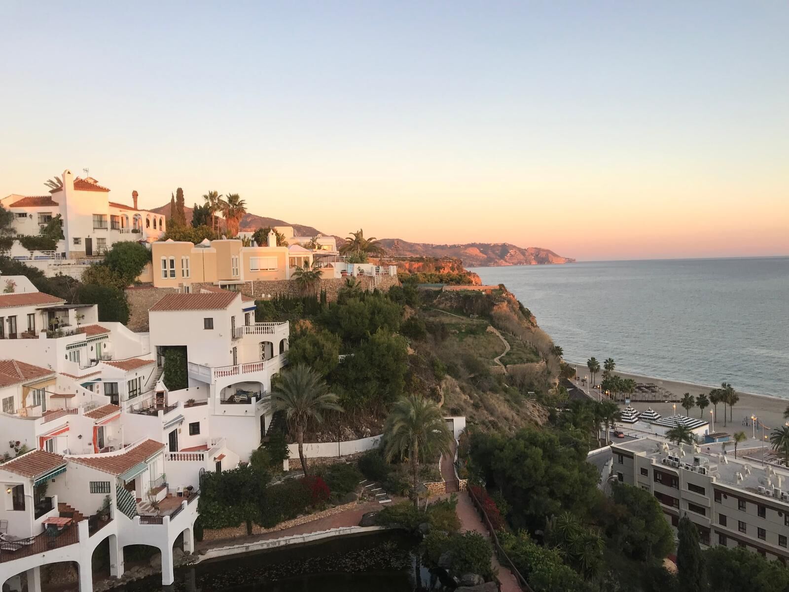 A coastal town with white buildings, a beach, and a clear sky.