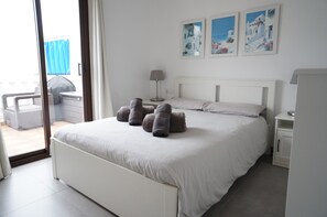 Ein Schlafzimmer mit Bett, Nachttisch, Lampe und Blick ins Freie.