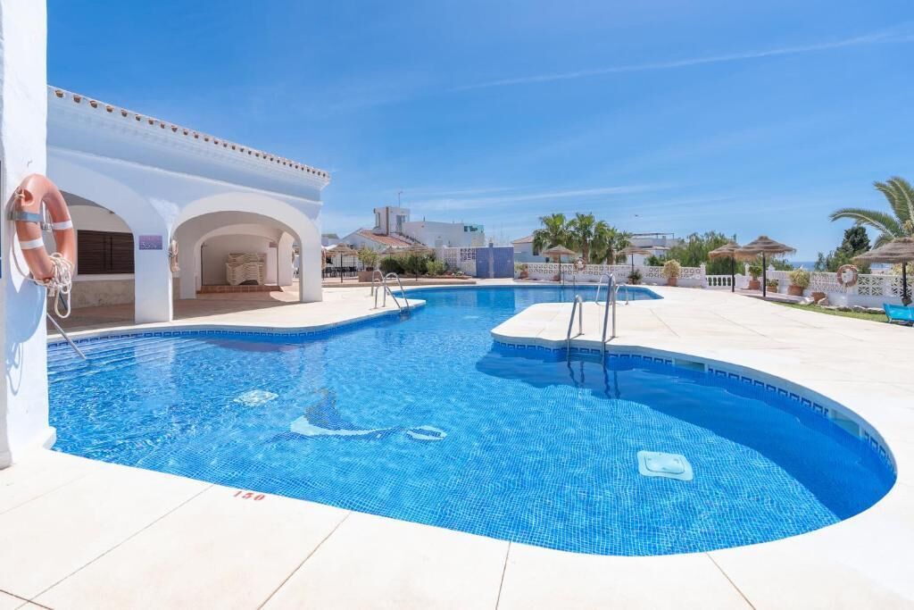 A swimming pool with clear blue water, a lifebuoy, and a white building with arches.