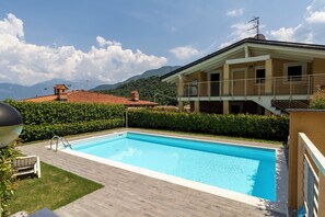 Une piscine avec une terrasse en bois, un banc et une vue sur les montagnes en arrière-plan.