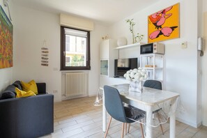 Un salon moderne comprenant un canapé, une table à manger avec des chaises, un coin cuisine équipé d’appareils électroménagers et une grande fenêtre.