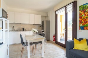 Une cuisine moderne avec des meubles blancs, une table à manger avec des chaises, un réfrigérateur et un extincteur.