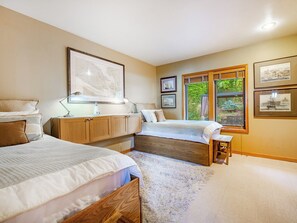 Een slaapkamer met twee bedden, een houten kast, een raam met uitzicht op groen en fotolijstjes aan de muur.