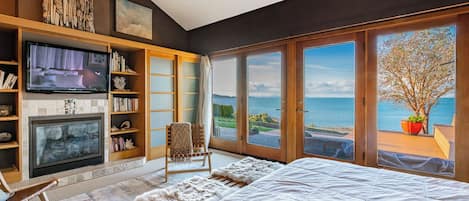 Une chambre avec un grand lit, une cheminée, une télévision et une vue sur la mer.