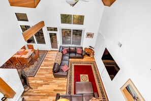 A spacious living area with a wooden floor, a sectional sofa, a dining table with chairs, and a red rug.