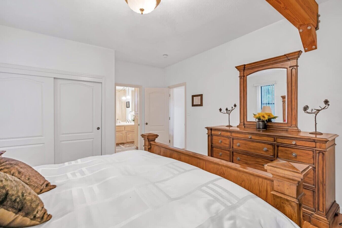A bedroom with a bed, dresser, mirror, and a door leading to a bathroom.