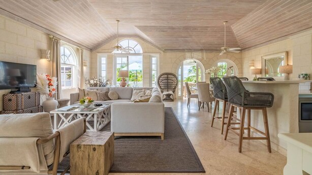Amplia sala de estar con sofá, mesa de centro, sillas, televisor y un área de cocina con taburetes de bar.