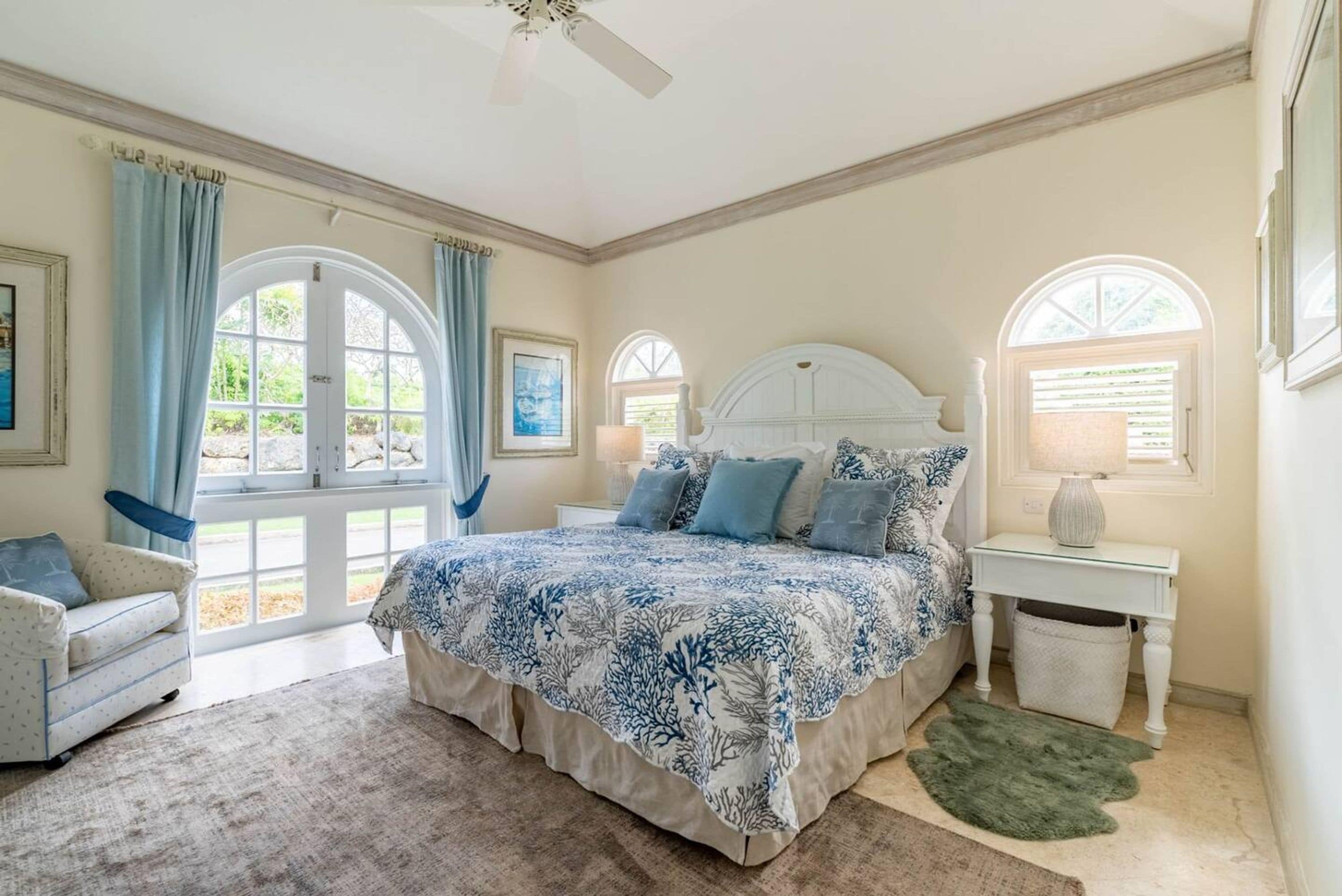 A bedroom with a large bed, two windows, a ceiling fan, and a view of the outdoors.