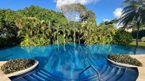 Una piscina azul cristalina con borde de azulejos, rodeada de abundante vegetación y palmeras.
