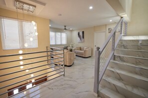 A spacious living area with a staircase, a sofa set, and a ceiling fan. - Horizon- 6BR Gated Villa Near Beach w Pool (Oistins)