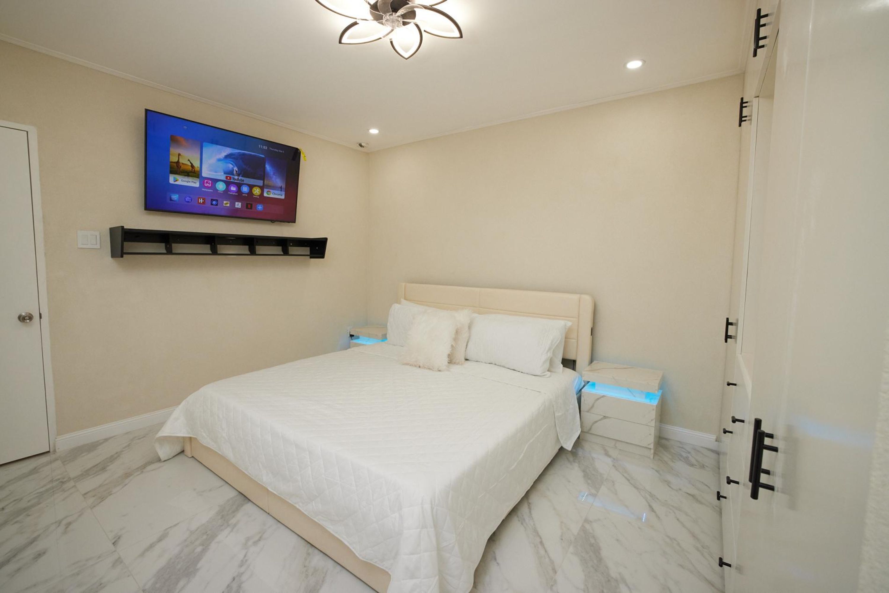 Een slaapkamer met een bed, een wandtelevisie, een plafondlamp en een deur.