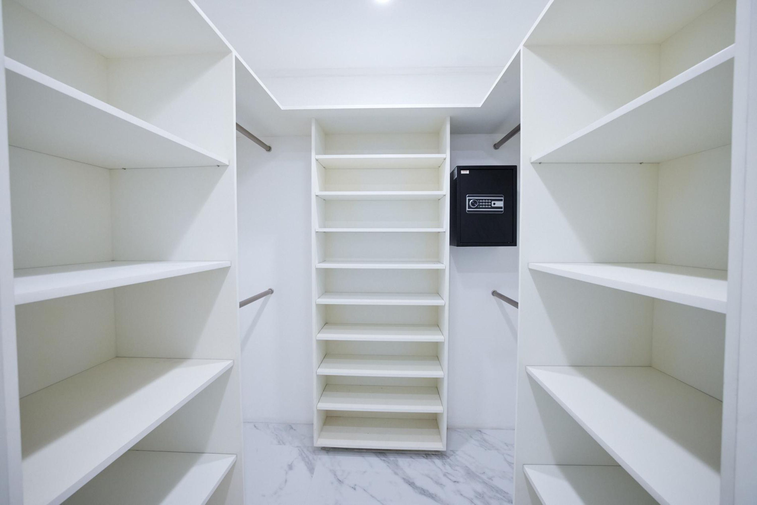 A walk-in closet with multiple shelves and a black electronic device on the wall.