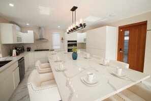 A modern kitchen with a marble countertop, built-in oven, and a long dining table with white chairs. - Horizon- 6BR Gated Villa Near Beach w Pool (Oistins)