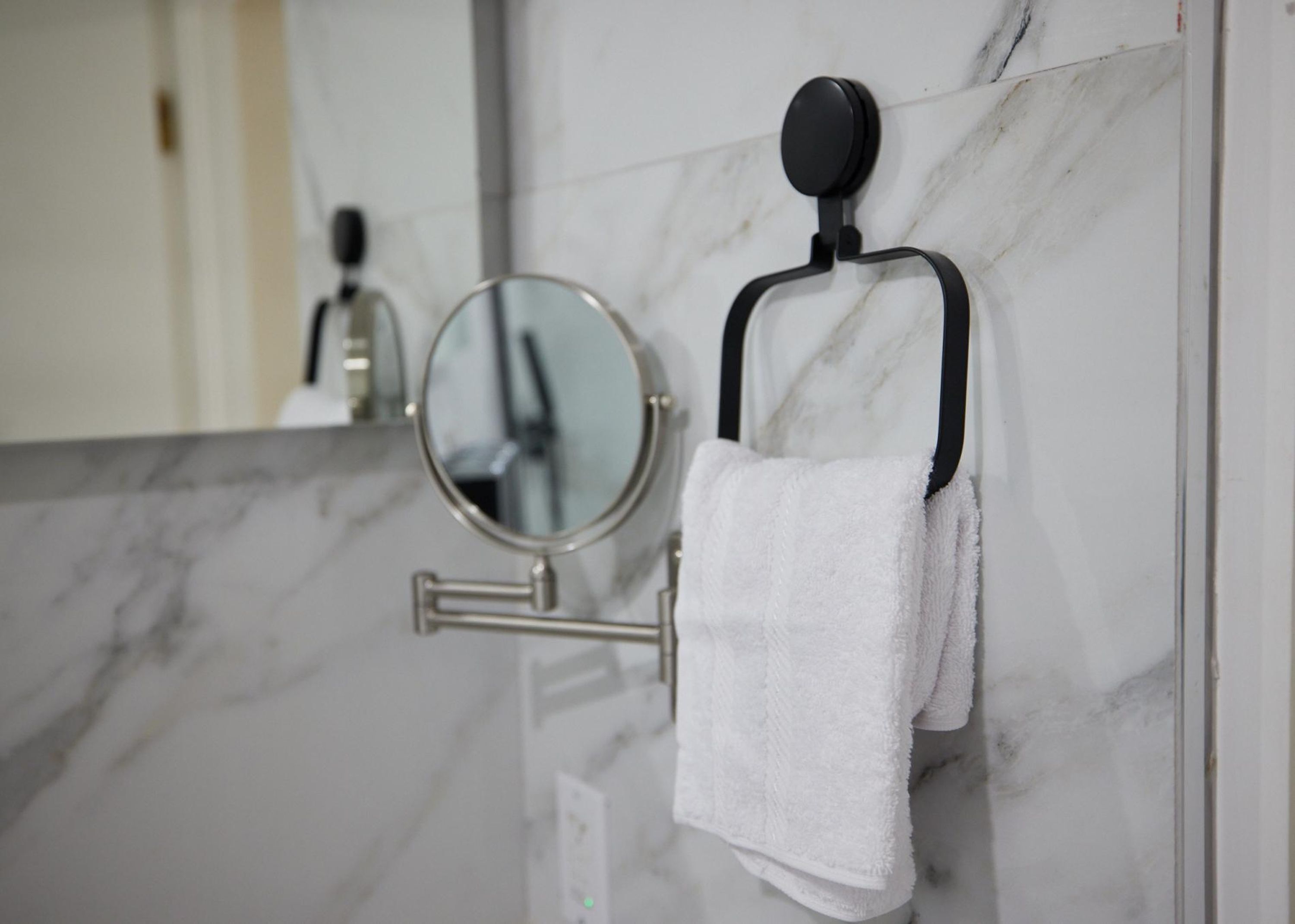 Un baño con pared de mármol, un perchero con una toalla blanca y un espejo.