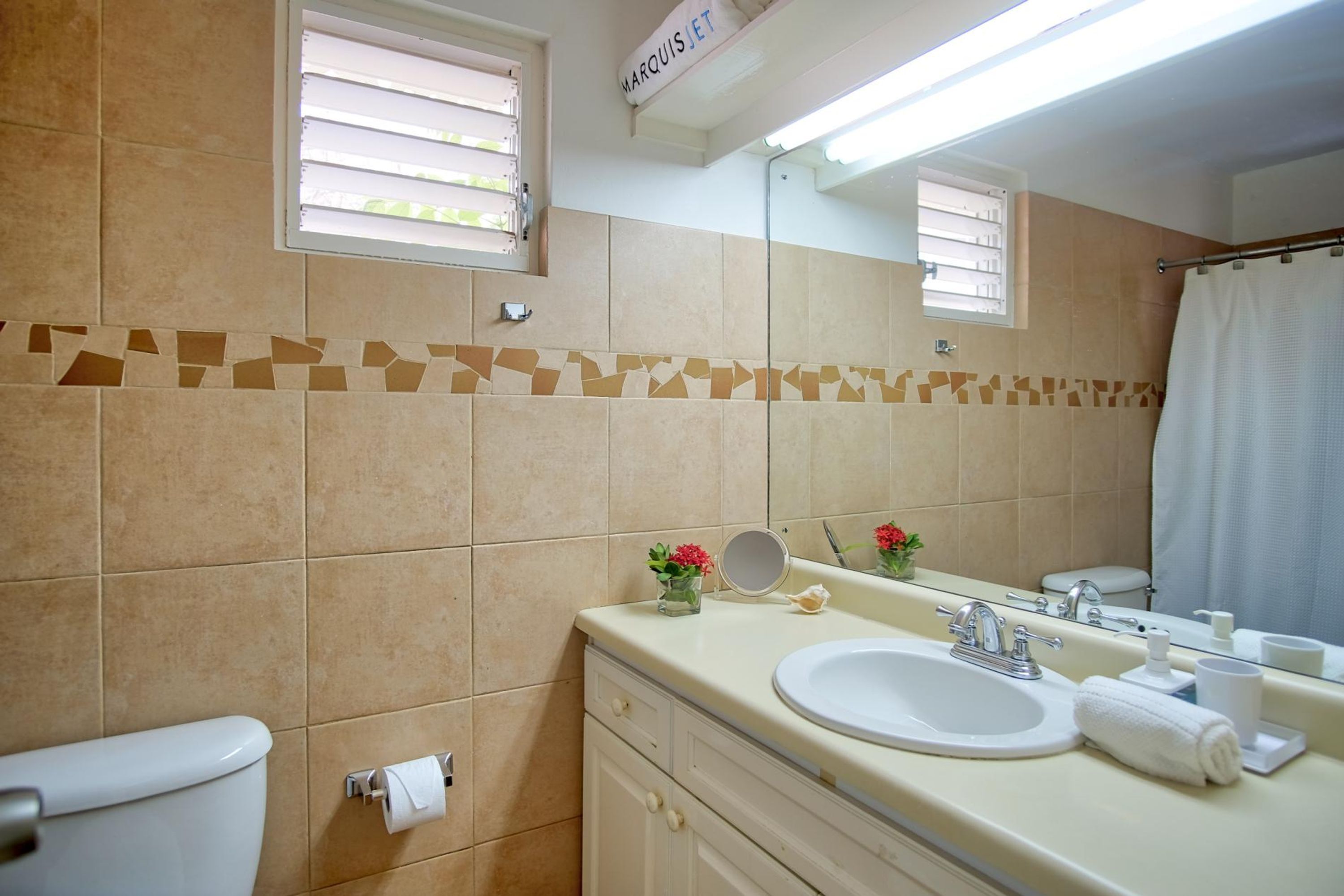 A bathroom with beige tiles, a toilet, a sink with a mirror, a towel rack, and a shower curtain.